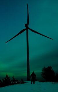 Silhouette of man by wind turbine on land against sky during winter
