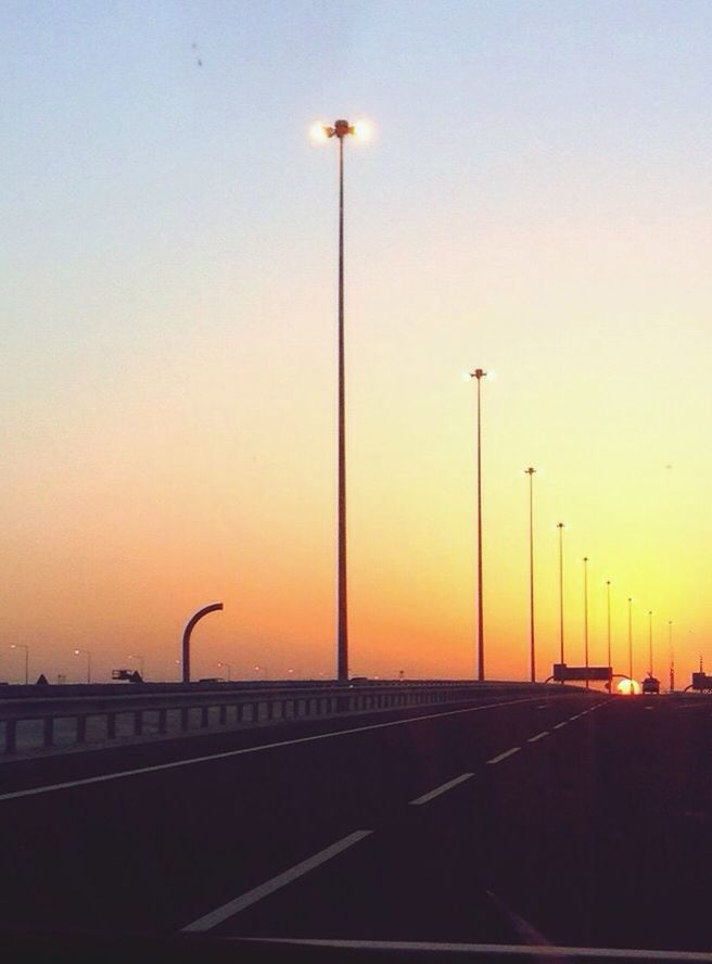 street light, sunset, transportation, lighting equipment, orange color, silhouette, clear sky, railing, the way forward, sky, road, illuminated, copy space, built structure, road marking, diminishing perspective, outdoors, street, no people, dusk