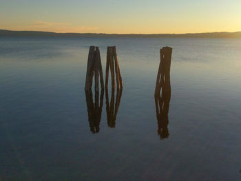 Wooden posts in lake against sky during sunset