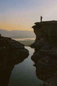 Man standing on cliff by sea against sky during sunset