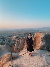 Portrait of young woman standing on rock against clear sky