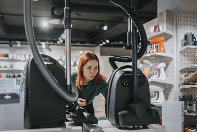 Female customer examining vacuum cleaner while shopping in modern electronics store