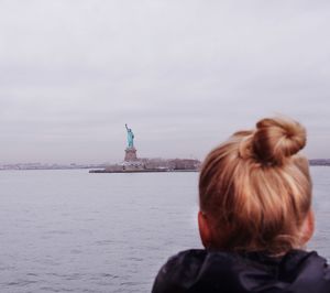 Rear view of woman sitting by sea looking at the statue of liberty 