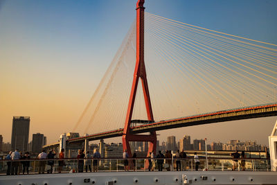 Suspension bridge in city against clear sky during sunset