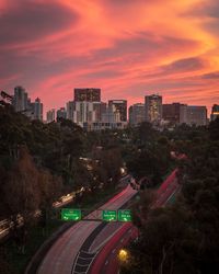 High angle view of light trails on road amidst buildings against sky during sunset