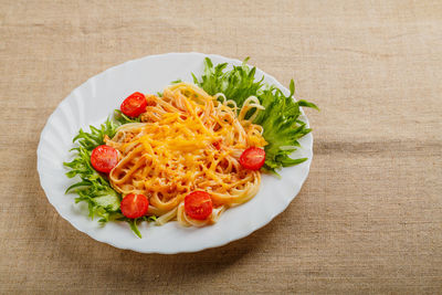 A plate of pasta with cherry tomatoes and cheese on a linen tablecloth. horizontal photo