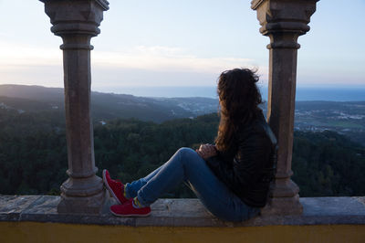 Woman sitting on column against sky