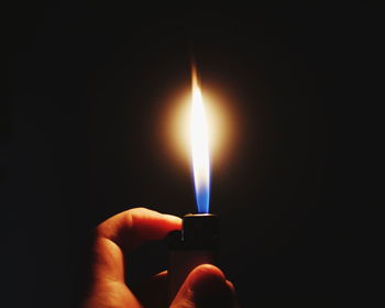 Close-up of hand holding lit candle against black background