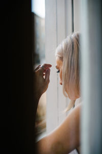 Side view of woman looking through window