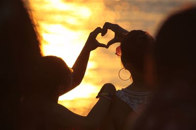 Women making a heart shape during sunset