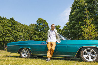 Young man with legs crossed at ankle standing near vintage car at park