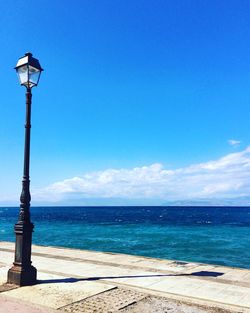 Street light by sea against blue sky