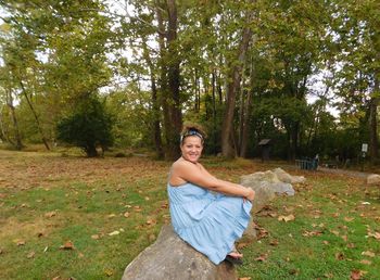 Portrait of smiling mature woman sitting on log in forest