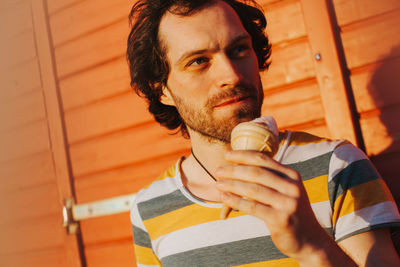 Close-up of man holding ice cream cone against wall