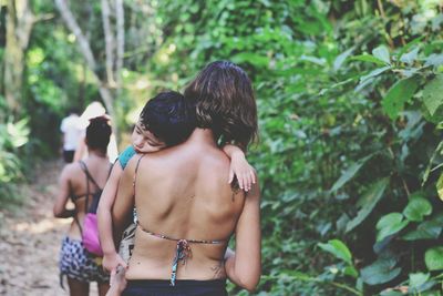 Rear view of mother carrying boy while walking in forest