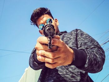 Low angle view of young man pointing gun against sky