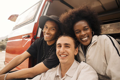 Portrait of smiling young man sitting with male and female friends in van