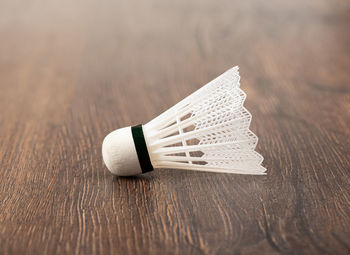 Lying on its side is a white plastic badminton shuttlecock on a wooden background.