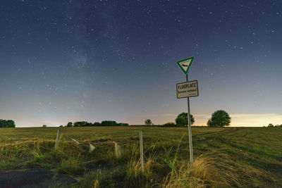 Road sign on field against sky