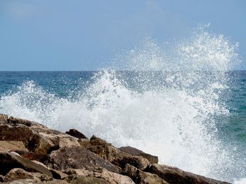 Waves splashing on rocks against sky