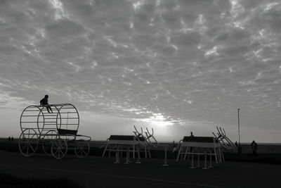 Silhouette man standing on bicycle by sea against sky during sunset