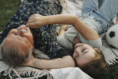 Smiling girl holding flower on grandfather's face while lying together