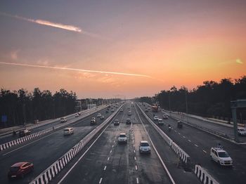 Cars on road in city against sky during sunset