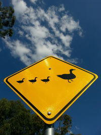 Low angle view of duck crossing road sign against sky