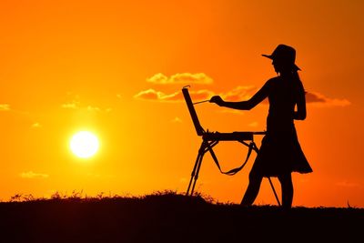 Silhouette of woman painting a picture at sunset