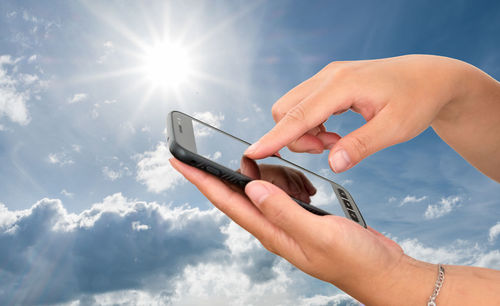Midsection of person using mobile phone against sky