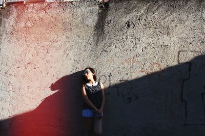 Young woman standing against wall on sunny day