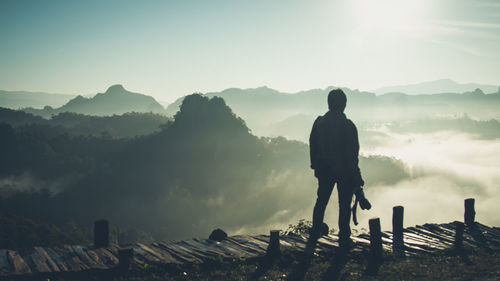 Man standing on boardwalk against mountains during foggy weather