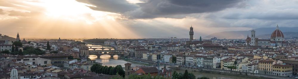 Panoramic shot of arno river amidst cityscape against sky during sunset