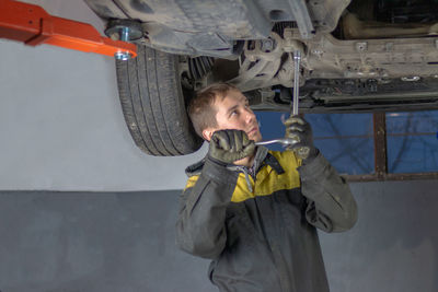 Young mechanic man working hard under the car in workshop garage