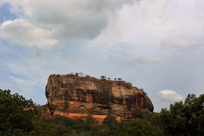 Low angle view of cliff against cloudy sky