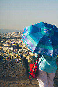 Rear view of man holding umbrella against sky in city