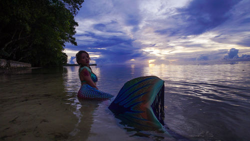 Woman sitting on beach against sky during sunset