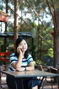 Young woman using phone while sitting on table