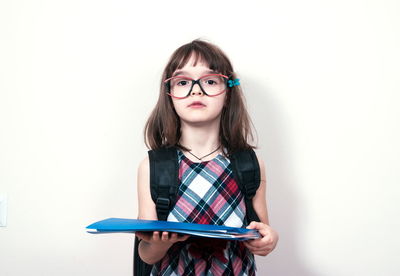 Portrait of young woman holding book while standing against white background