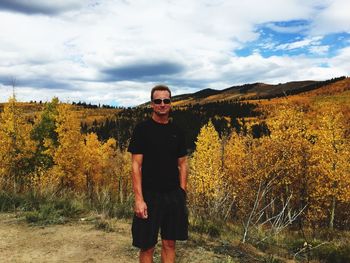 Portrait of mature man wearing sunglasses standing on landscape against cloudy sky