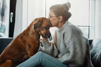 Side view of woman kissing dog while sitting at home