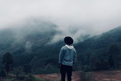 Rear view of man standing on field against sky during foggy weather