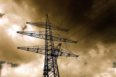 Low angle view of silhouette electricity pylon against cloudy sky