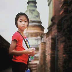 Low angle portrait of young woman standing against sky in city