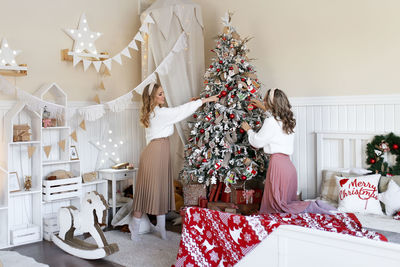 Two cute pretty girls sisters in cozy sweaters celebrate christmas in decorated bedroom of the house