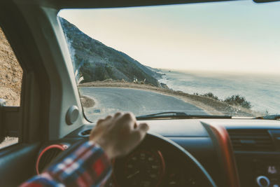 Cropped image of man driving car on road by sea