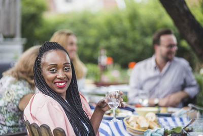 Portrait of smiling woman having wine while sitting with friends at garden party