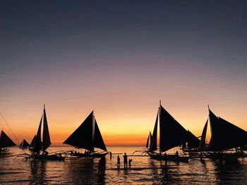 Silhouette sailboat sailing on sea against orange sky