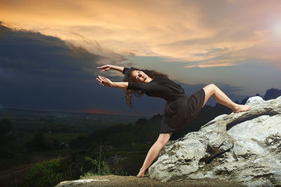 Young woman lying on rock against sky during sunset