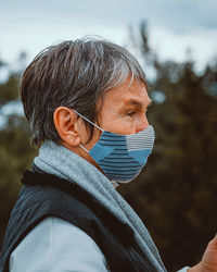 Portrait of an elder woman wearing surgical mask on nature background.